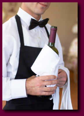 Waiter in tuxedo apron serving a bottle of wine.